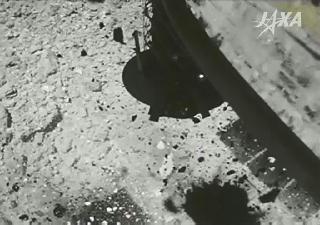 探査機「はやぶさ２」が小惑星「リュウグウ」に着地した直後の画像。舞い上がった岩石と、機体の一部（右）が映っている（ＪＡＸＡ提供）