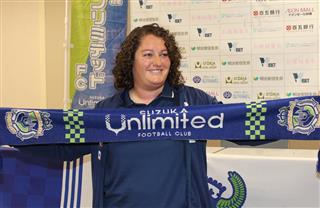 チーム名の入ったタオルを広げて写真撮影に応じるミラグロス監督＝鈴鹿市のイオンモール鈴鹿（写真をクリックすると他の写真も見られます）