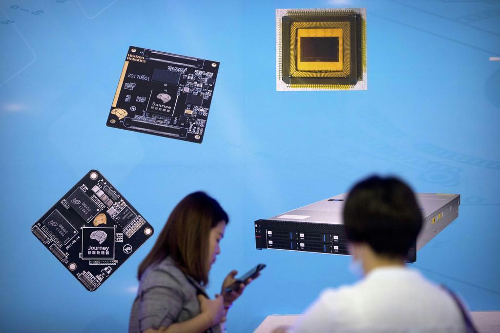 昨年５月、北京で開かれた国際ハイテクエキスポでマイクロチップや基盤を投影した展示の前を行く人々。中国はこの４０年間、外国企業に技術を引き渡すよう圧力をかけてきた。貿易相手国によると、うまくいかなかったら中国は望むものを盗んだと述べた（ＡＰ）