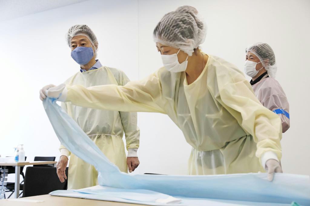 ＡＮＡグループの社員が医療用ガウンの検品を行う作業現場を視察する西村経済再生相（左奥）＝１日午前、東京都内