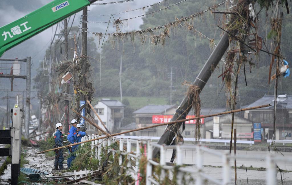 増水した川の水に倒された電柱の復旧工事にあたる人たち＝６日午前、熊本県球磨村