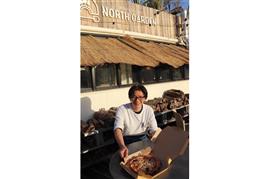 間伐材で焼いたピザが主役のカフェ「ノースガーデン」をまとめる田村直樹料理長。背後に積まれた薪のディスプレイも特徴的＝大阪府吹田市の万博記念公園