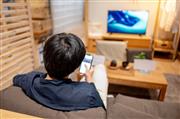 リビングで、テレビを見ながらスマホを操作する男性（画像はイメージです/Getty Images）